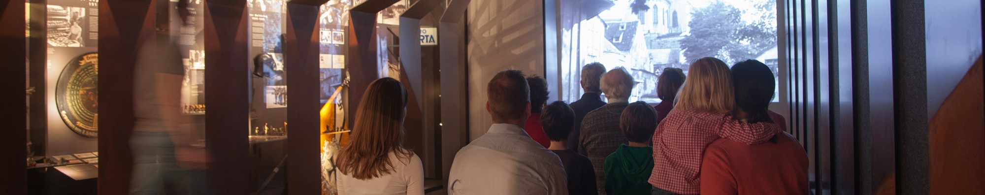 Besucher sitzen im Kino der Dauerausstellung. Links sind die Vitrinen &uuml;ber die Geschichte des 20. Jahrhunderts.