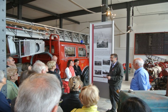 Mitglieder des Freundeskreises vor einem alten L&ouml;schfahrzeug, lauschen der F&uuml;hrung eines Herrn