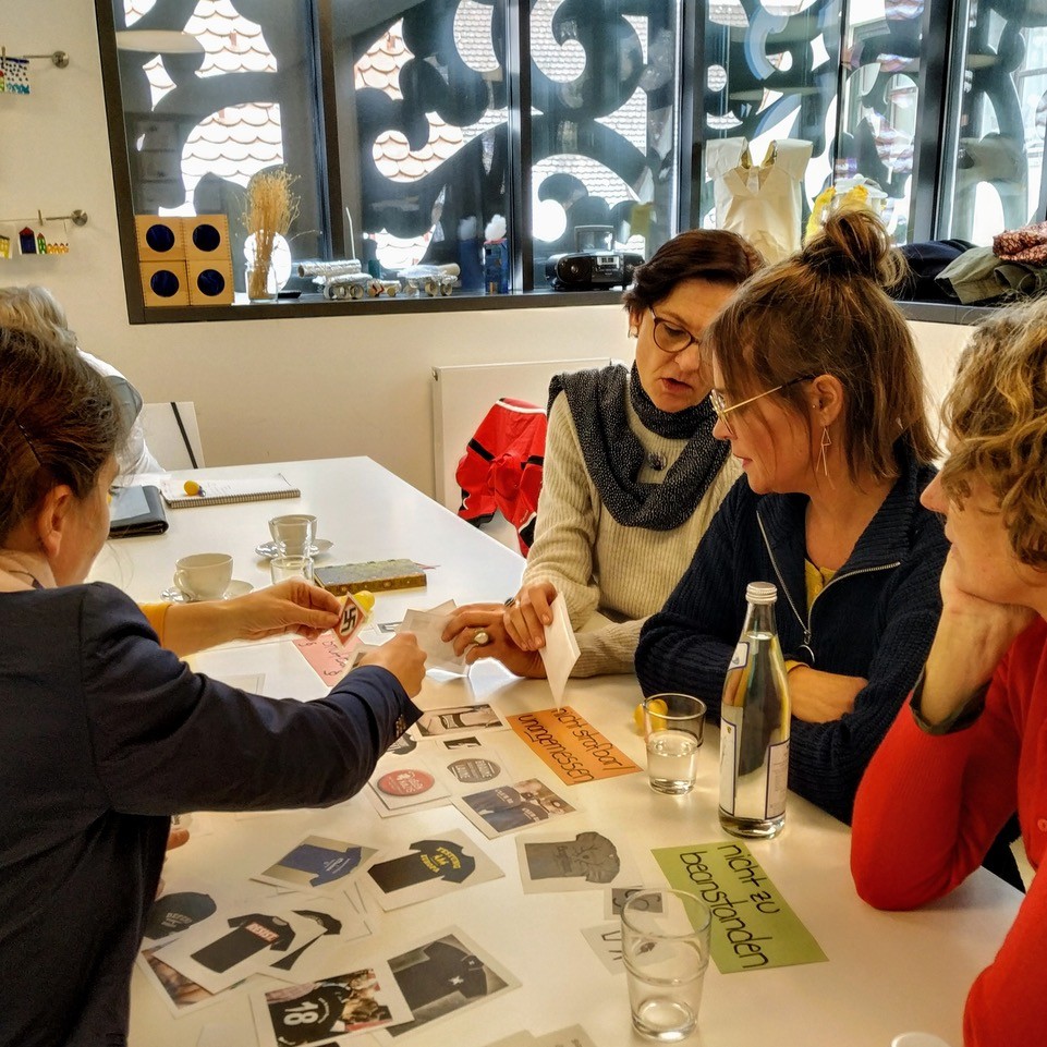 Workshop: vier Frauen sitzen an einem Tisch und besch&auml;ftigen sich mit verschiedenen rechtsextremen Symbolen, die auf Papierstreifen ausgeschnitten sind