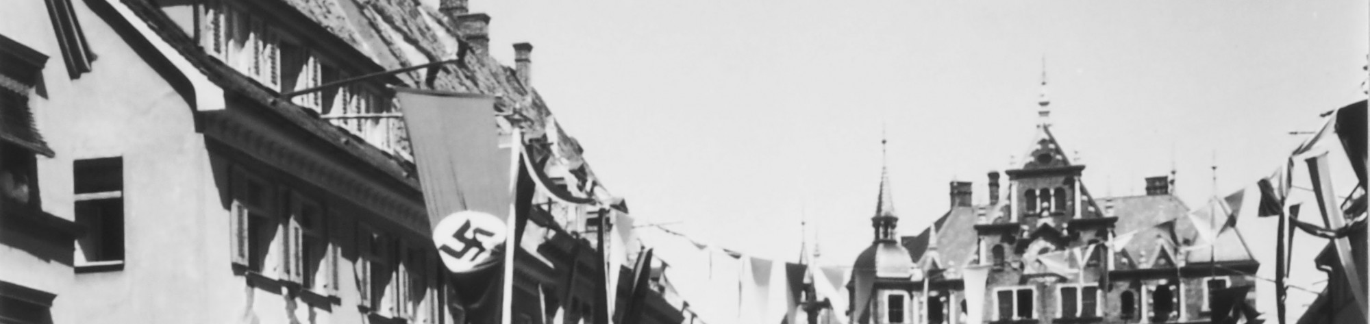Teilansicht eines Fotos. Zu sehen sind die D&auml;cher der Geb&auml;ude in der Kaiser-Max-Stra&szlig;e, darunter des Rathauses. Au&szlig;erdem sind Girlanden und eine Hakenkreuzfahne aufgeh&auml;ngt.