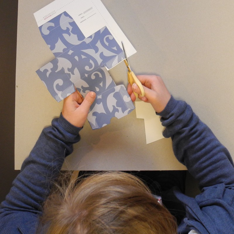 Kind von oben schneidet die Umrisse einer Schachtel aus