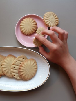 Eine Hand stibitzt einen Osterkeks von einem Teller. Daneben ist ein weiterer Teller mit eierf&ouml;rmigen Keksen