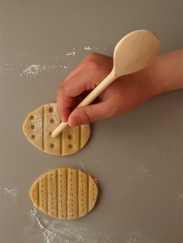 Die eierf&ouml;rmig ausgestochenen Kekse werden mit der R&uuml;ckseite eines Kochl&ouml;ffels mit Mustern eingedr&uuml;ckt