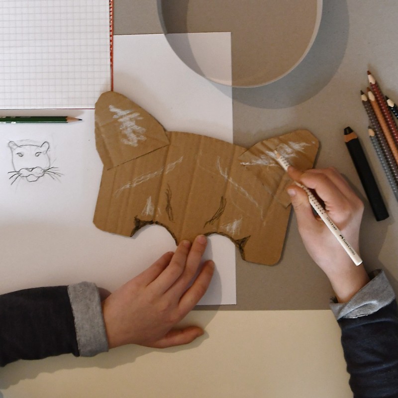 Zwei H&auml;nde bemalen eine "Katzen-Maske"