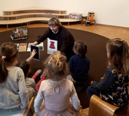 Eine Frau zeigt einer Gruppe Kindern verschiedene Karten mit Kleidungsst&uuml;cken darauf.