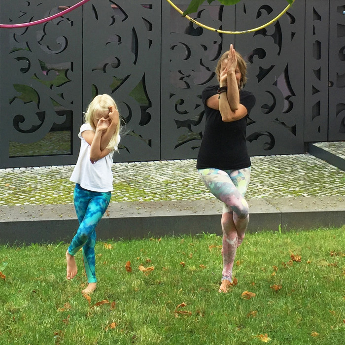 Eine Frau und ein Kind machen im Museumsgarten die Yoga-Figur "Der Adler"