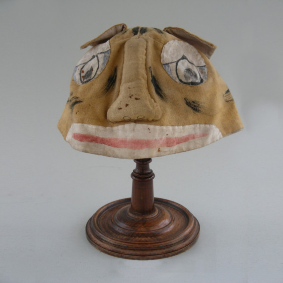 Beige Faschingsmaske mit gro&szlig;er Nase, gro&szlig;em Mund und gro&szlig;en Augen auf einem Holzst&auml;nder