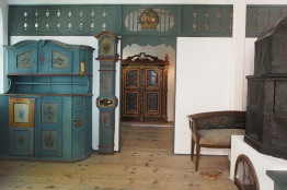 Blick in die Blaue Stube, links ein alter blauer Bauernschrank, rechts ein Ofen, daneben eine Bank mit einem "Stiefelknecht davor"