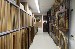 Museumsdepot, links ein Regal, in das Bilder einsortiert sind, rechts h&auml;ngen Bilder an einer Gitterwand.