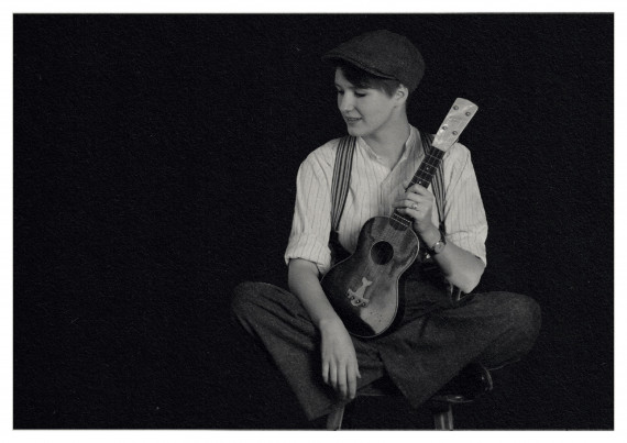Schwarz/wei&szlig;-Foto, eine junge Frau, sitzend, gekleidet im Stil der 1920er Jahre, h&auml;lt eine Ukulele in der linken Hand