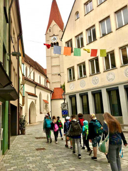 Eine Gruppe von Jugendlichen mit Rucksack an gehen zwischen H&auml;user in Richtung einer Kirche
