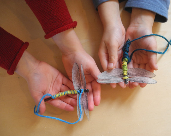 Die Hände von zwei Kindern halten jeweils einen gebastelten Schmetterling.