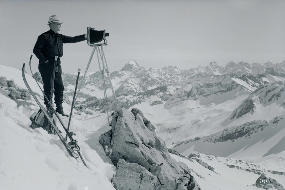 Mann mit Skiern und Plattenkamera in verschneiten Bergen.