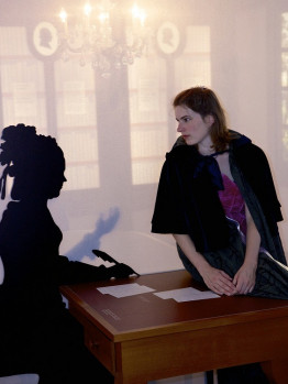 Eine Frau im Umhang sitzt auf dem Schreibtisch mit der Silhouette von Sophie von La Roche.